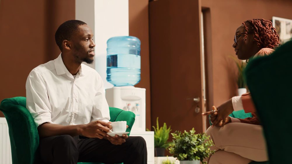 Two people talking in a counselling lounge with green armchairs