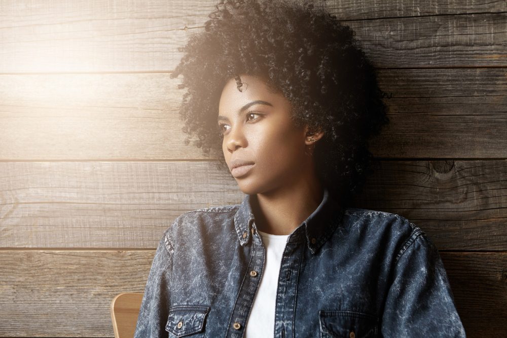 Thoughtful young woman looking into the distance against a wooden wall